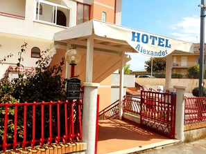 A hotel entrance with a sign reading "HOTEL Alexander," a red gate, and a lamp post. - Hotel Alexander (Giardini Naxos)