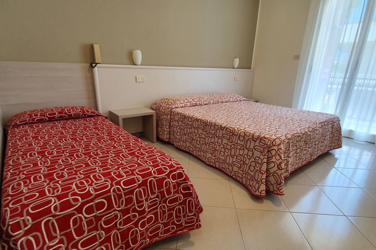 A hotel room with two beds, a small bedside table, and a window with curtains.