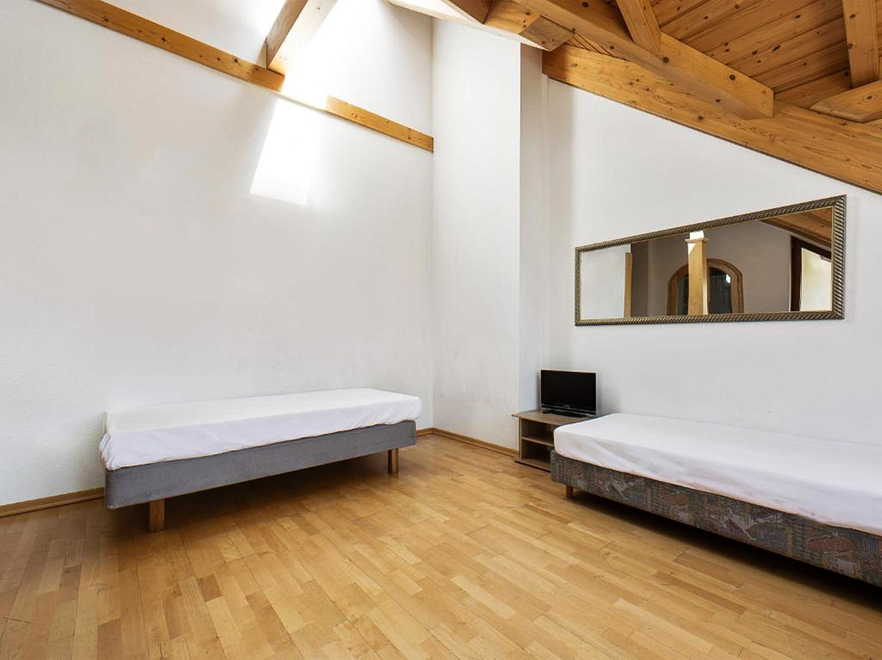 Ein Zimmer mit zwei Betten, Holzboden, Spiegel und Fernseher.