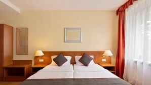 Une chambre d’hôtel avec deux lits, une tête de lit en bois, des lampes de chevet, un miroir et une fenêtre avec des rideaux.