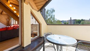 Une terrasse sur le toit avec un plafond en bois, une porte vitrée donnant sur un balcon, une table ronde en métal et des coussins rouges sur un canapé.