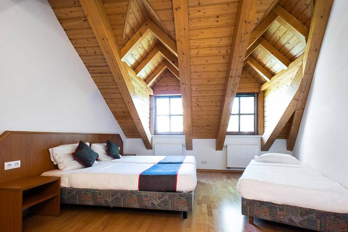 Una habitación con dos camas, vigas de madera, un ventanal y un radiador.