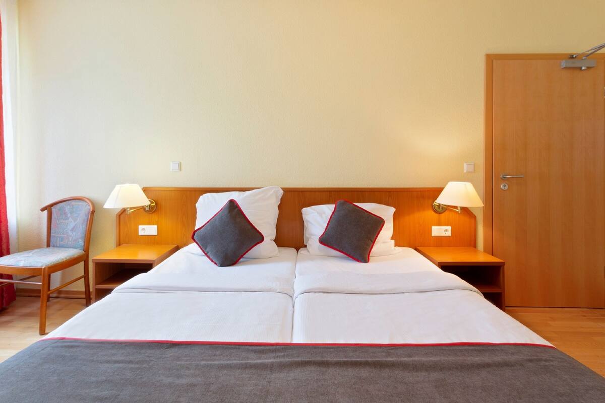 Habitación de hotel con una cama grande, dos mesitas de noche, dos lámparas, una silla y una puerta de madera.