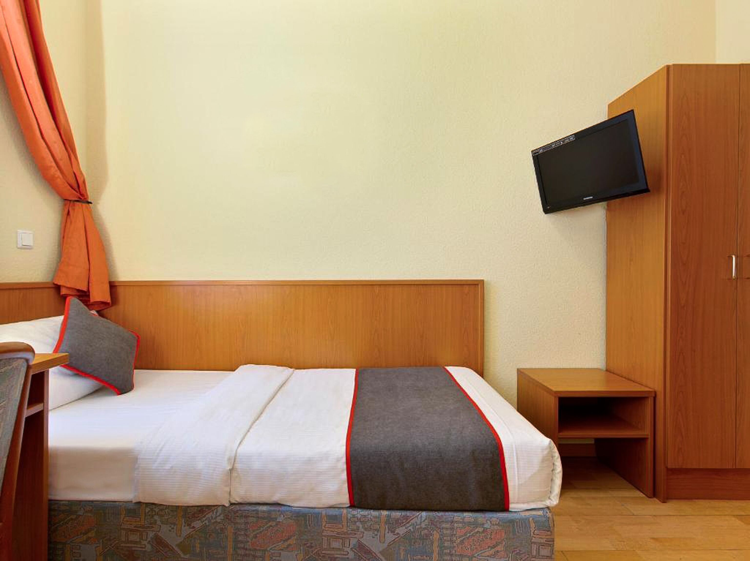 A hotel room with a bed, a TV mounted on the wall, and a wardrobe.
