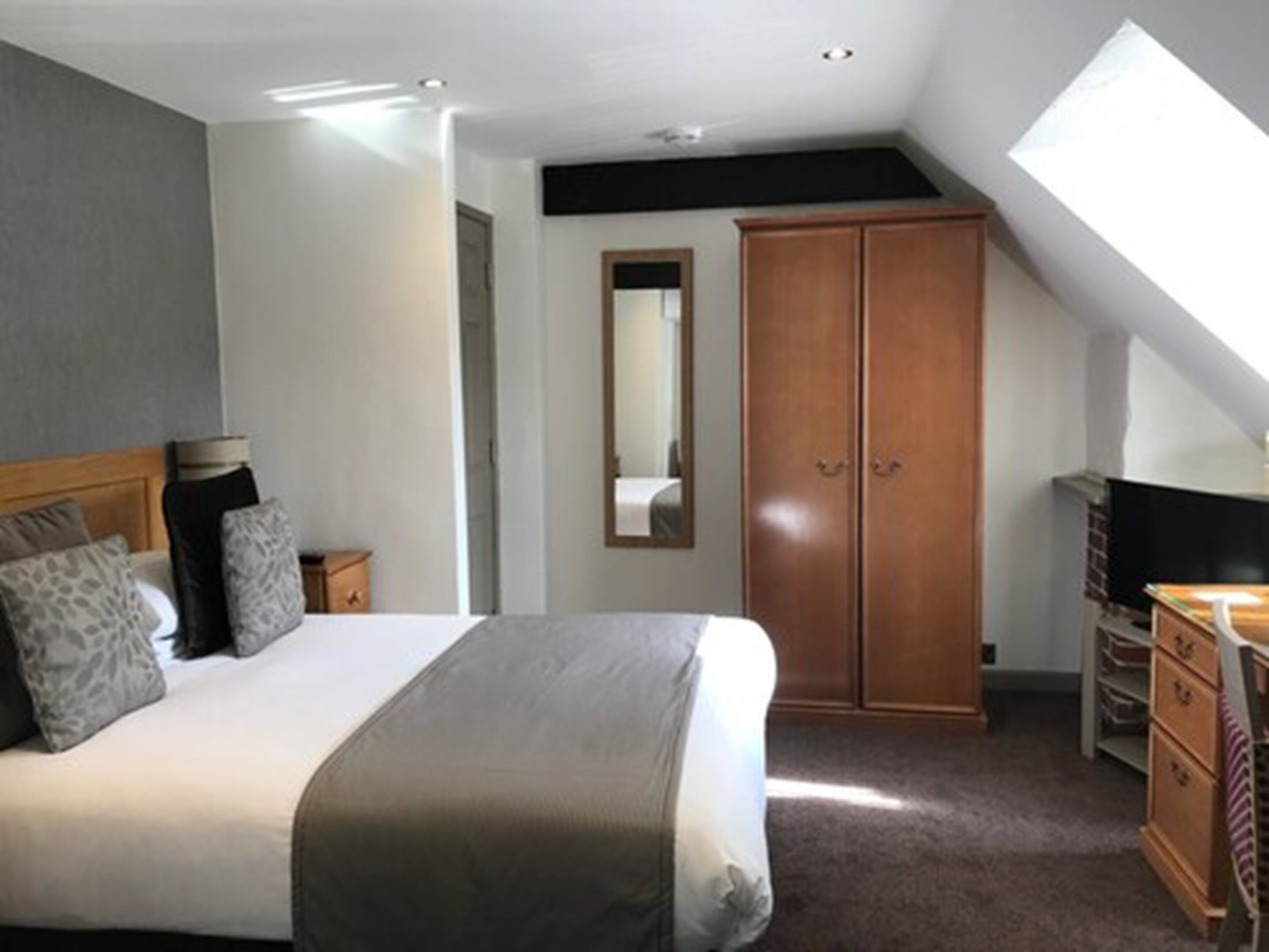 A bedroom with a bed, a wardrobe, a mirror, and a television.