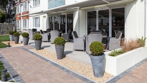 Un edificio residencial moderno con un patio cubierto, mobiliario exterior y plantas en macetas.
