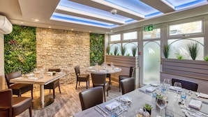 A restaurant with a stone wall and greenery, a round table set for dining, and a skylight ceiling. - La Barbarie Hotel by Eight Continents (St. Martins)