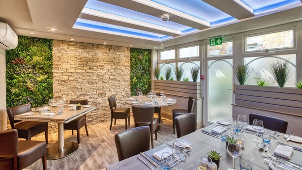 A restaurant with a stone wall and greenery, a round table set for dining, and a skylight ceiling. - La Barbarie Hotel by Eight Continents (St. Martins)