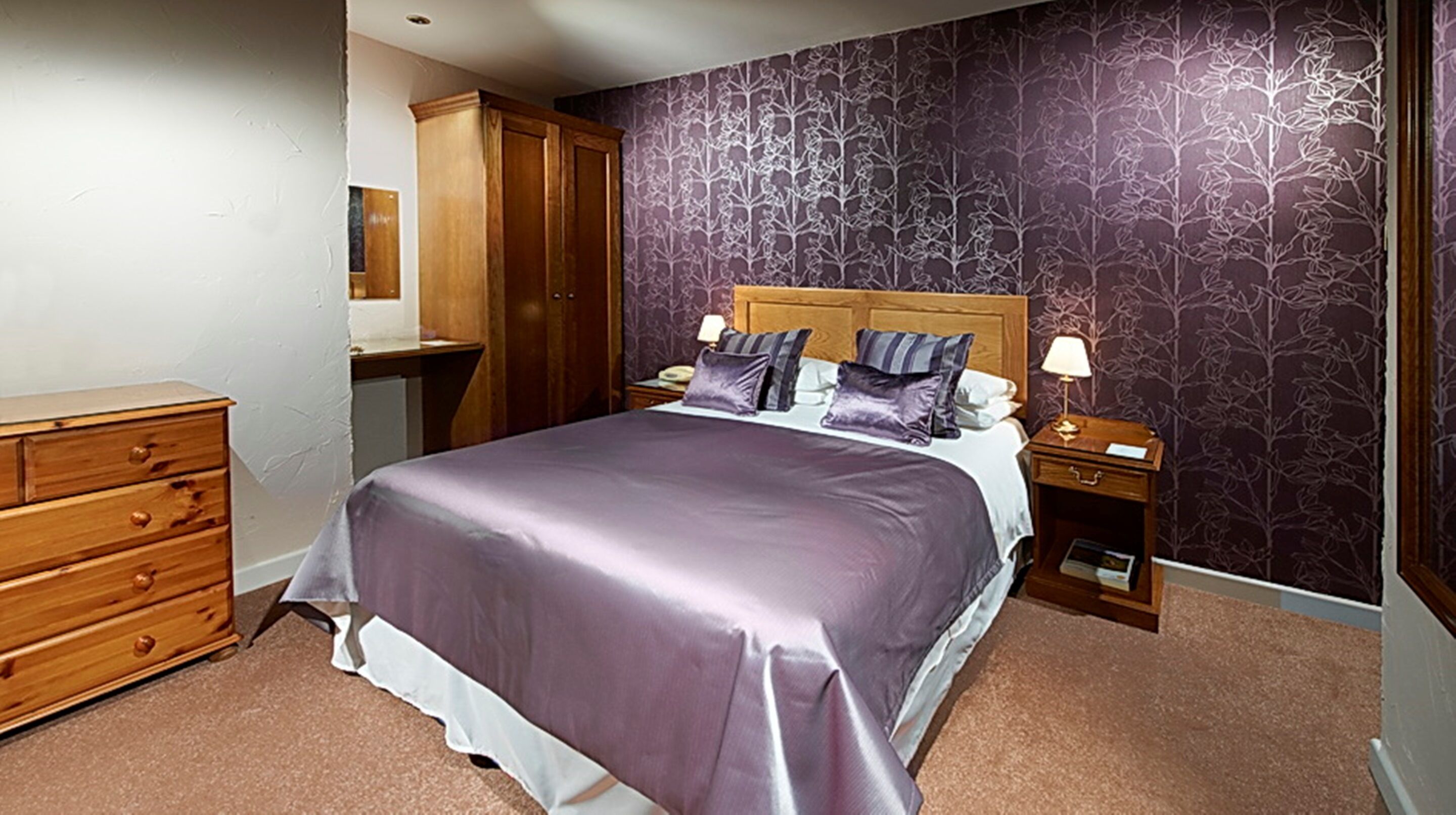 A bedroom with a large bed, wooden wardrobe, and a nightstand with a lamp.