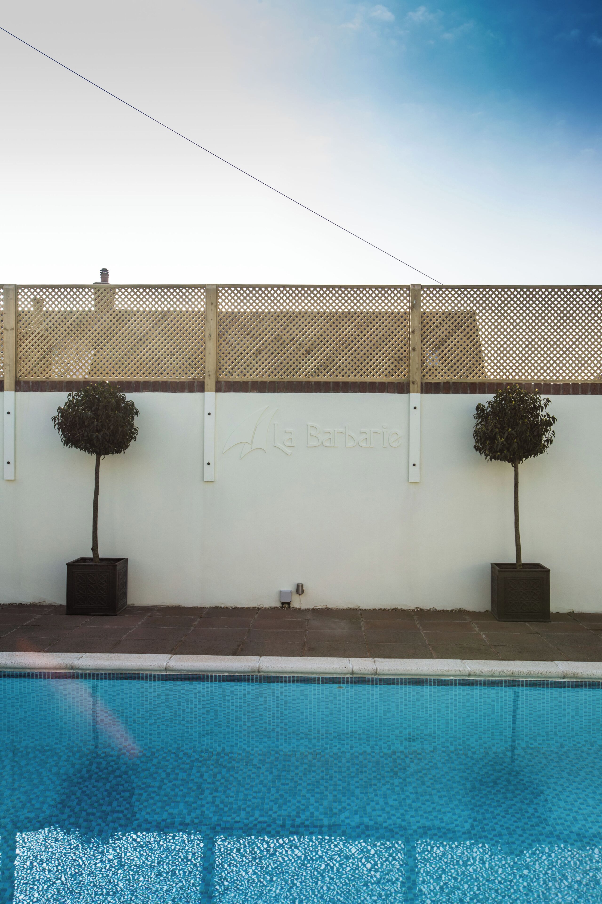 A swimming pool with two potted trees and a wall with the inscription "La Barbatie".