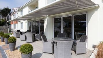An outdoor patio area with wicker furniture, a round table, and potted plants.