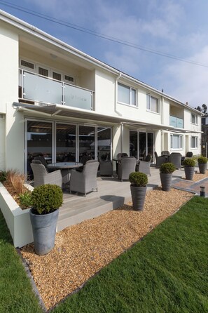 A modern building with a covered patio area featuring outdoor furniture and potted plants.