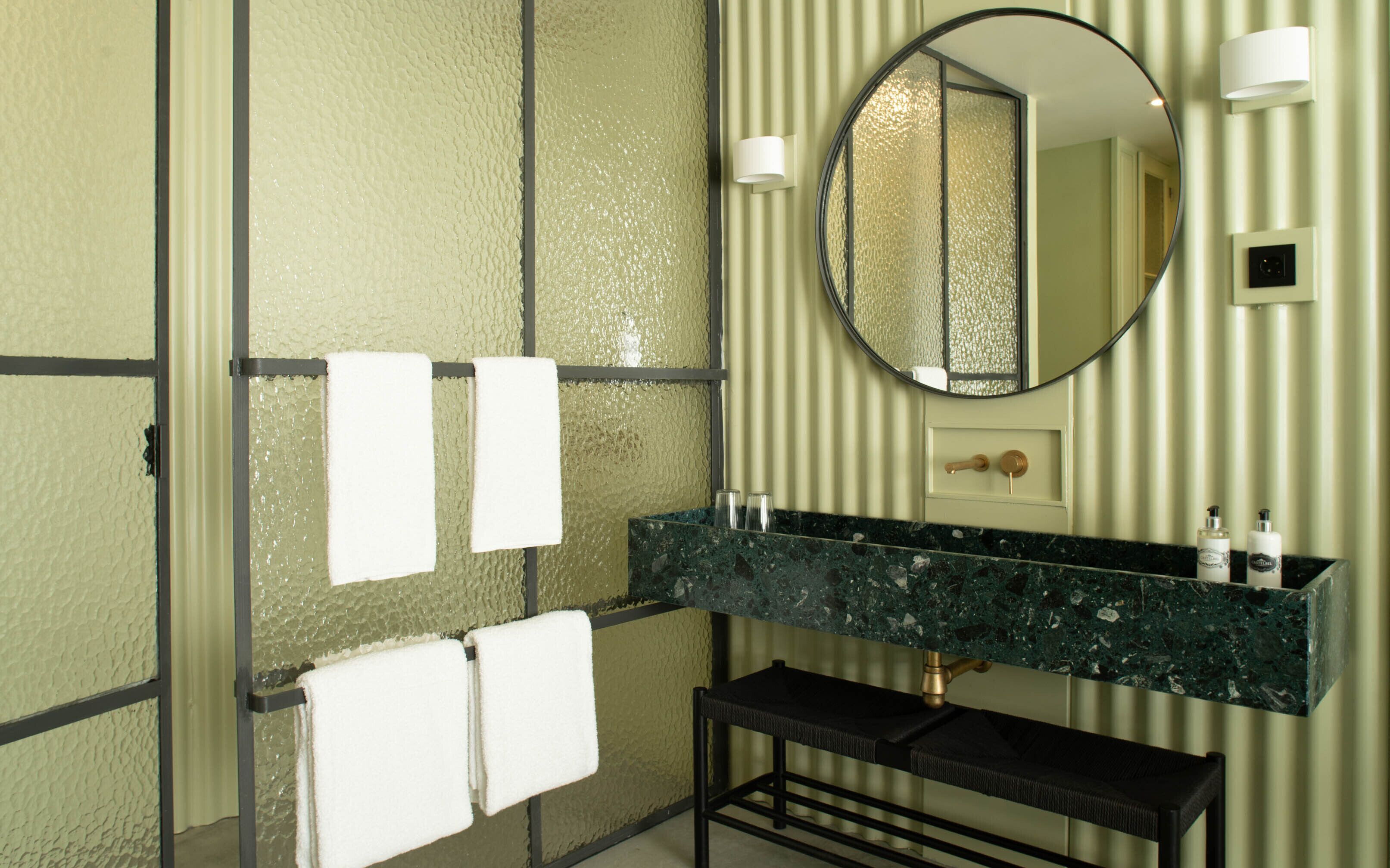 A bathroom with a marble sink, a round mirror, and two towels hanging on a towel rack.