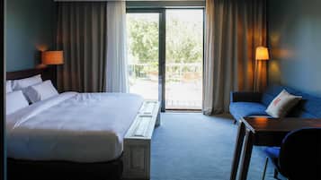 A hotel room with a large bed, a sofa, a small table, and a view of the outdoors through a sliding door.