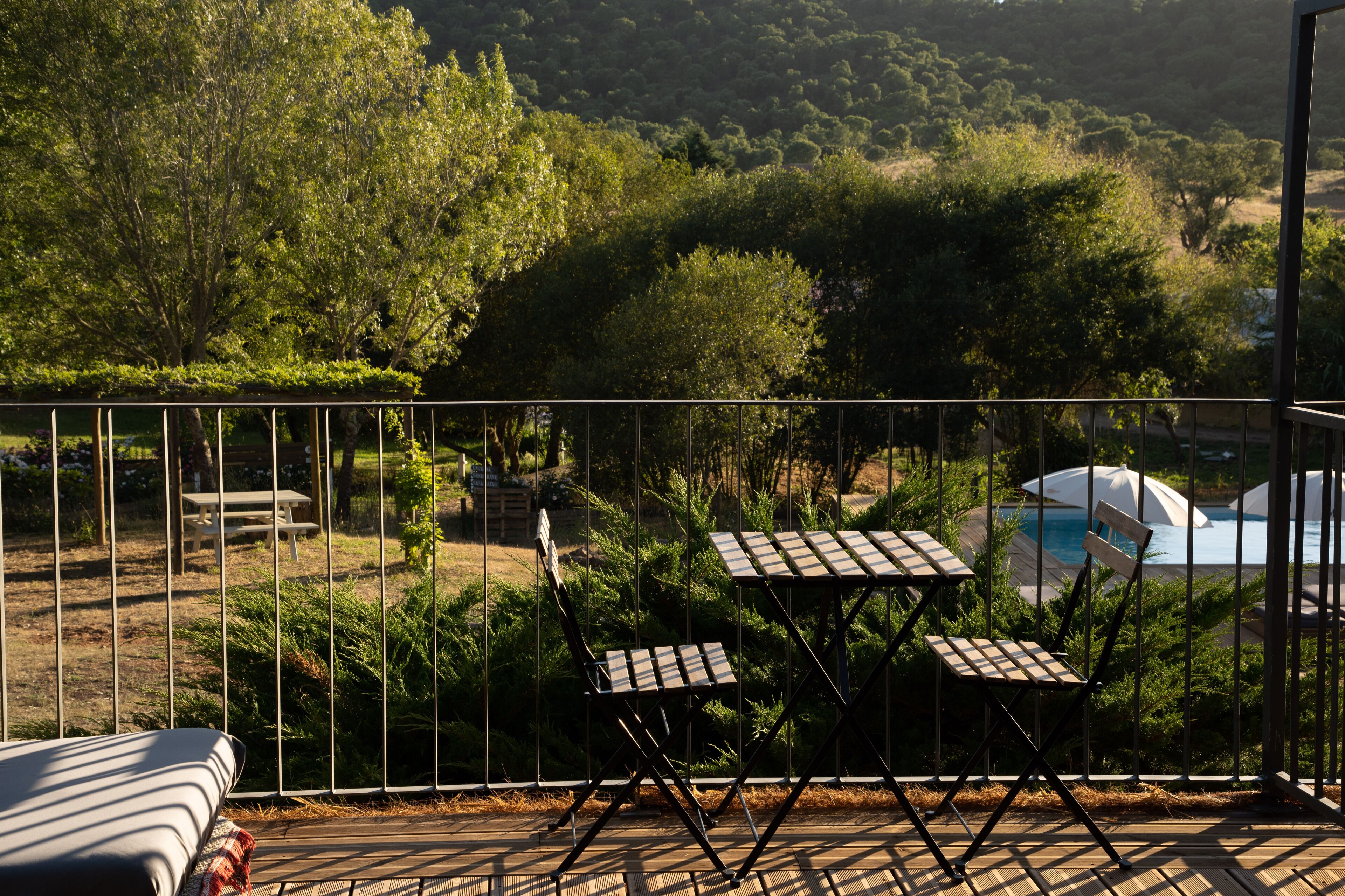A deck with two tables and chairs, overlooking a pool and lush greenery.