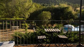 A deck with two tables and chairs, overlooking a pool and lush greenery.