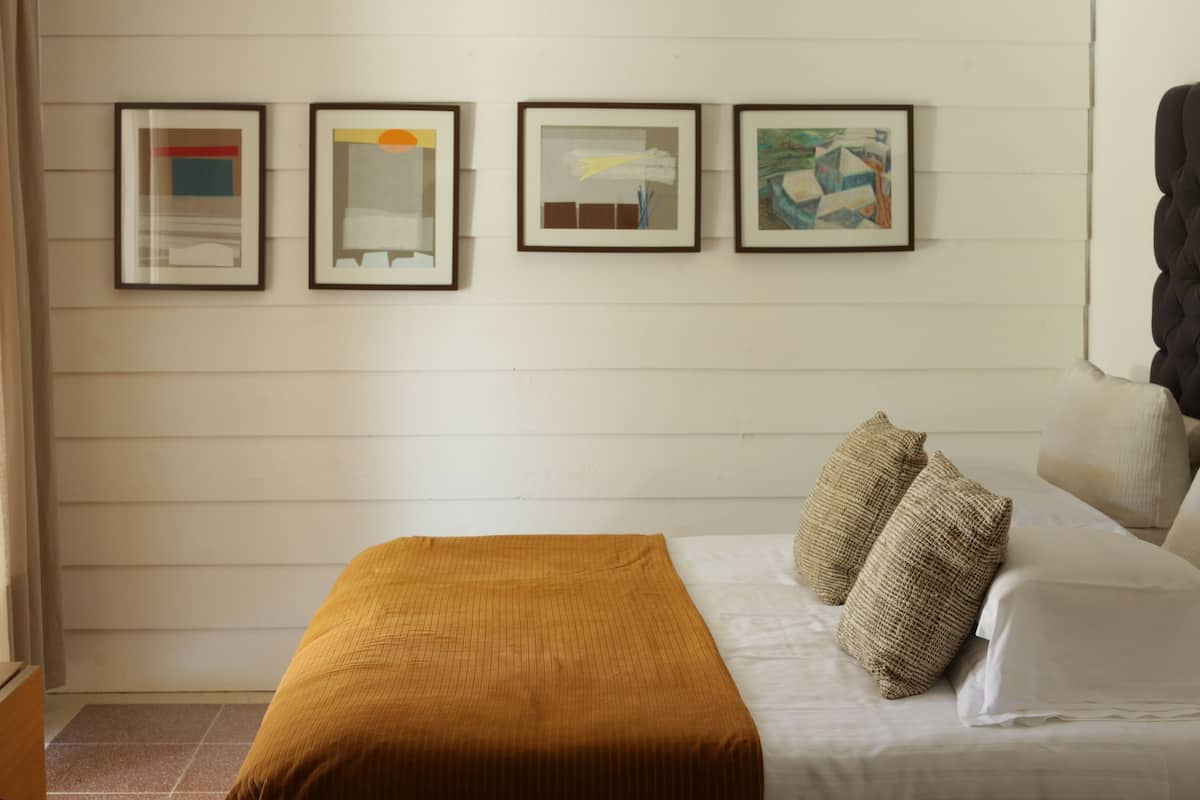 A bedroom with a bed, a brown blanket, and four framed artworks on the wall.