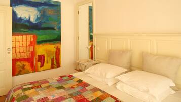 Un dormitorio con un cuadro grande y colorido en la pared, una colcha acolchada y un cabecero blanco.