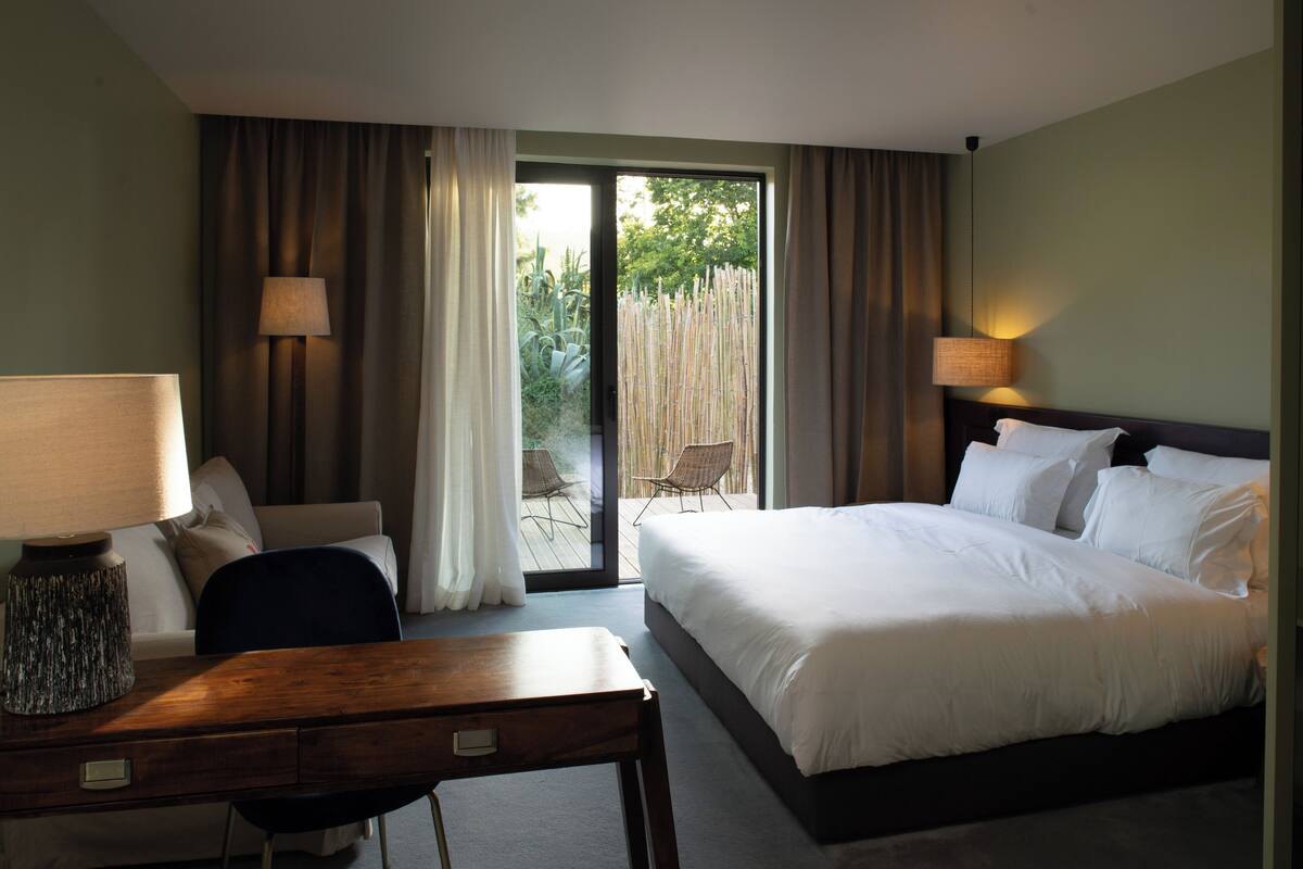 A hotel room with a bed, a desk, a chair, and a view of the outdoors.