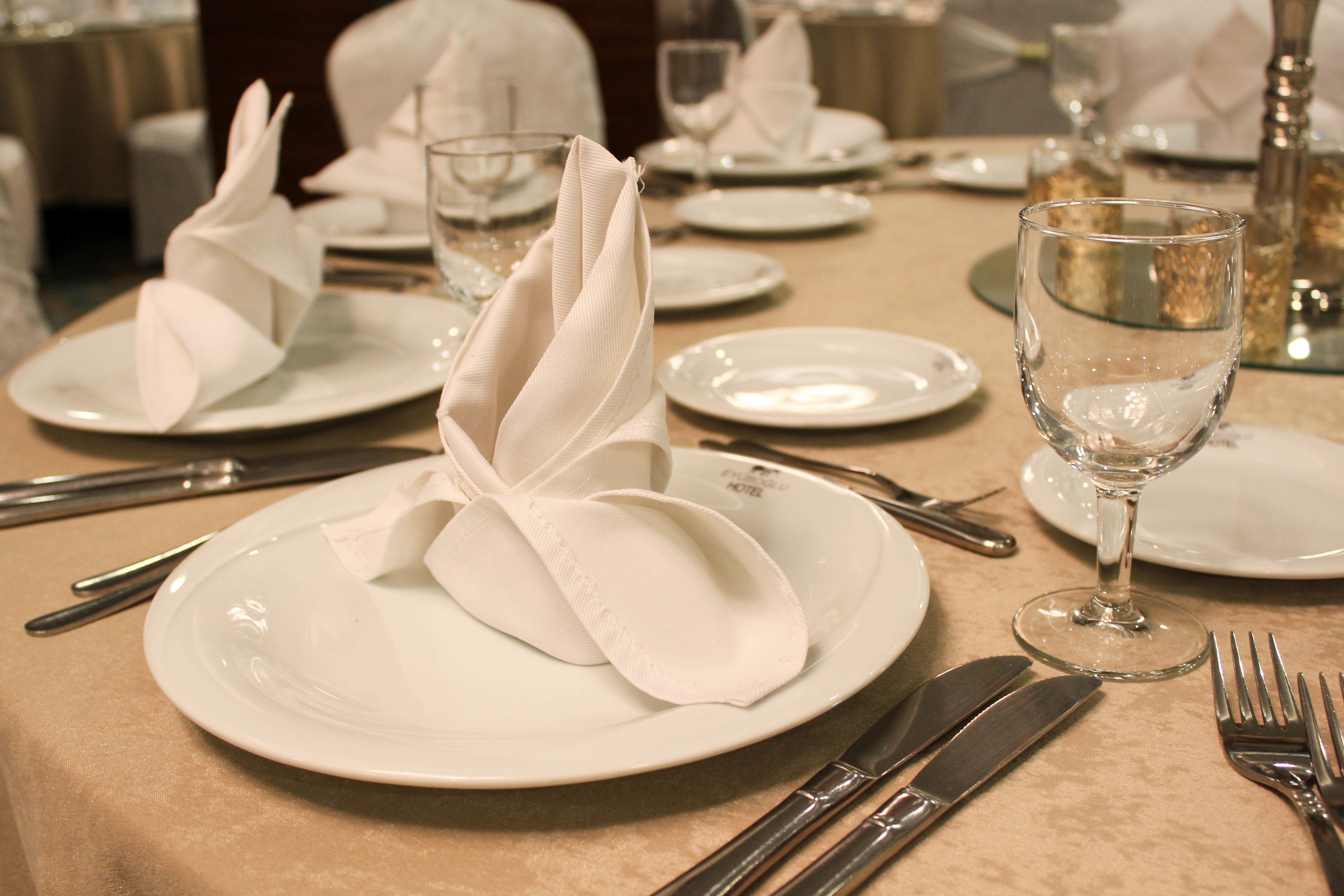 Mesa lista para comer, con platos blancos, servilletas dobladas y cubiertos.