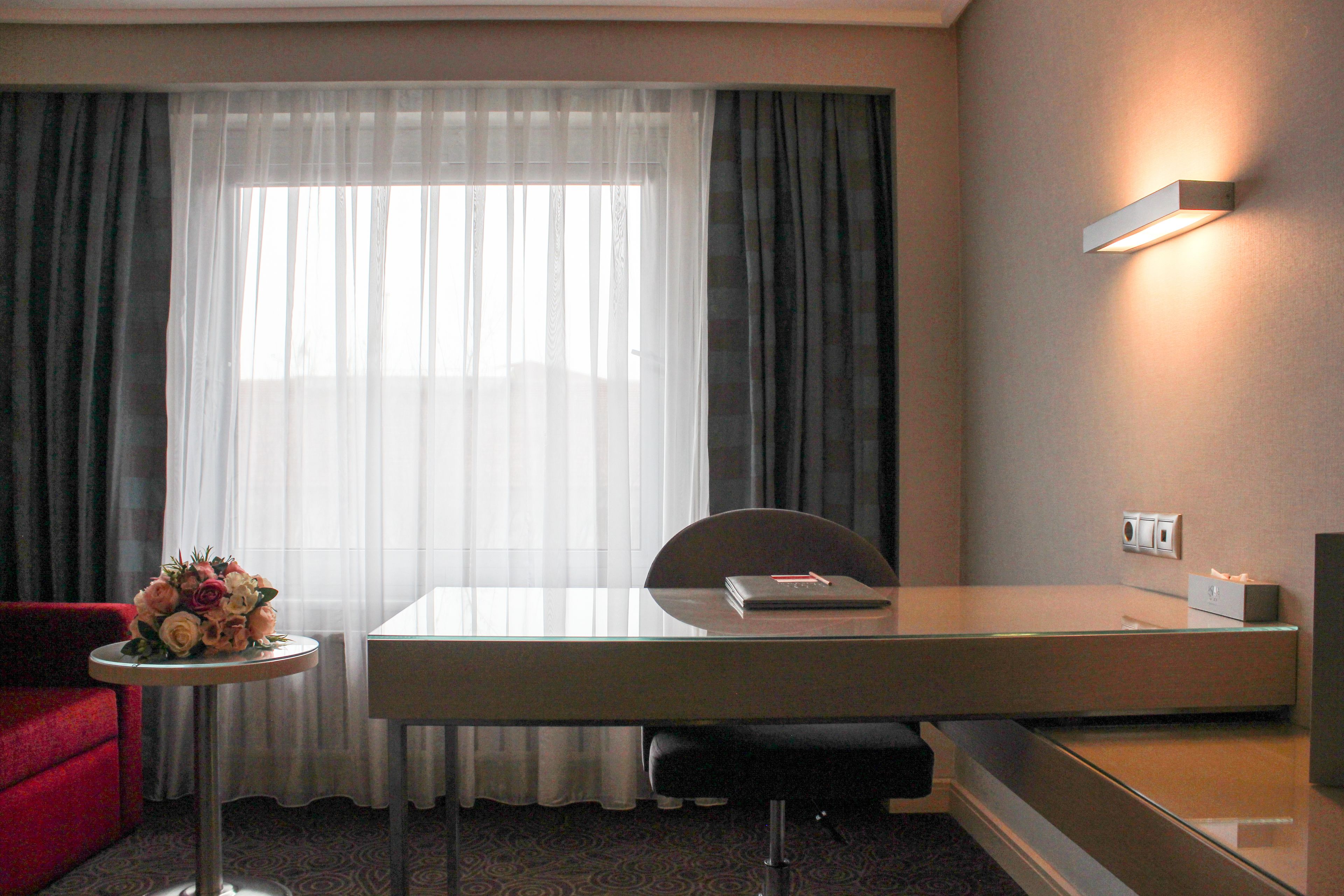 A hotel room with a desk, chair, and a small table with a bouquet of flowers.