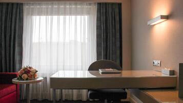 A hotel room with a desk, chair, and a small table with a bouquet of flowers.