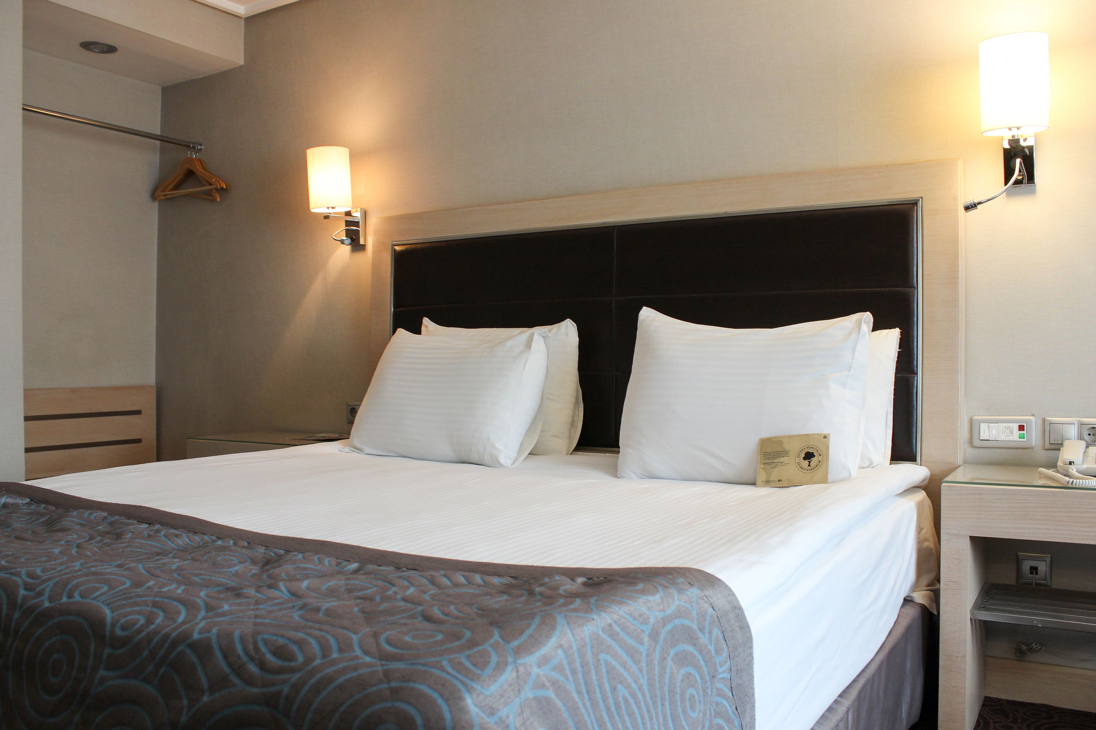 A hotel room with a large bed, two bedside lamps, a bedside table, and a wardrobe.