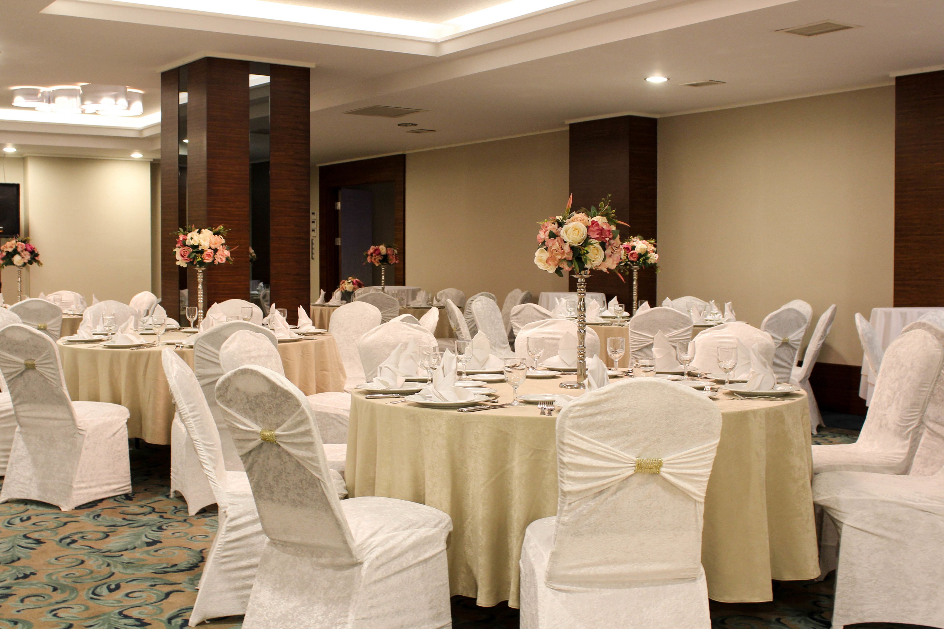 A banquet hall with round tables, white chairs, and floral centerpieces.