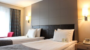 Habitació d'hotel amb dos llits, una cadira vermella, una taula de nit amb un telèfon i una làmpada fixa a la paret.