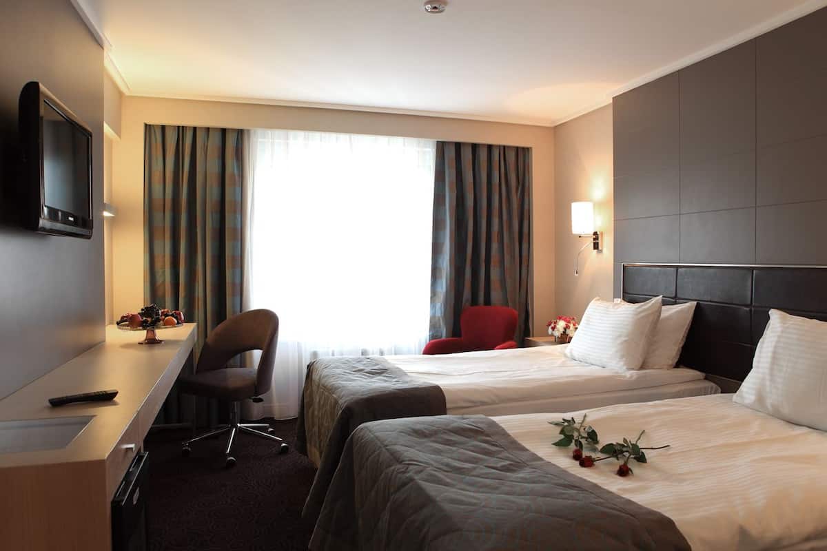 Habitación de hotel con dos camas, un escritorio, un televisor, una silla y una ventana con cortinas.