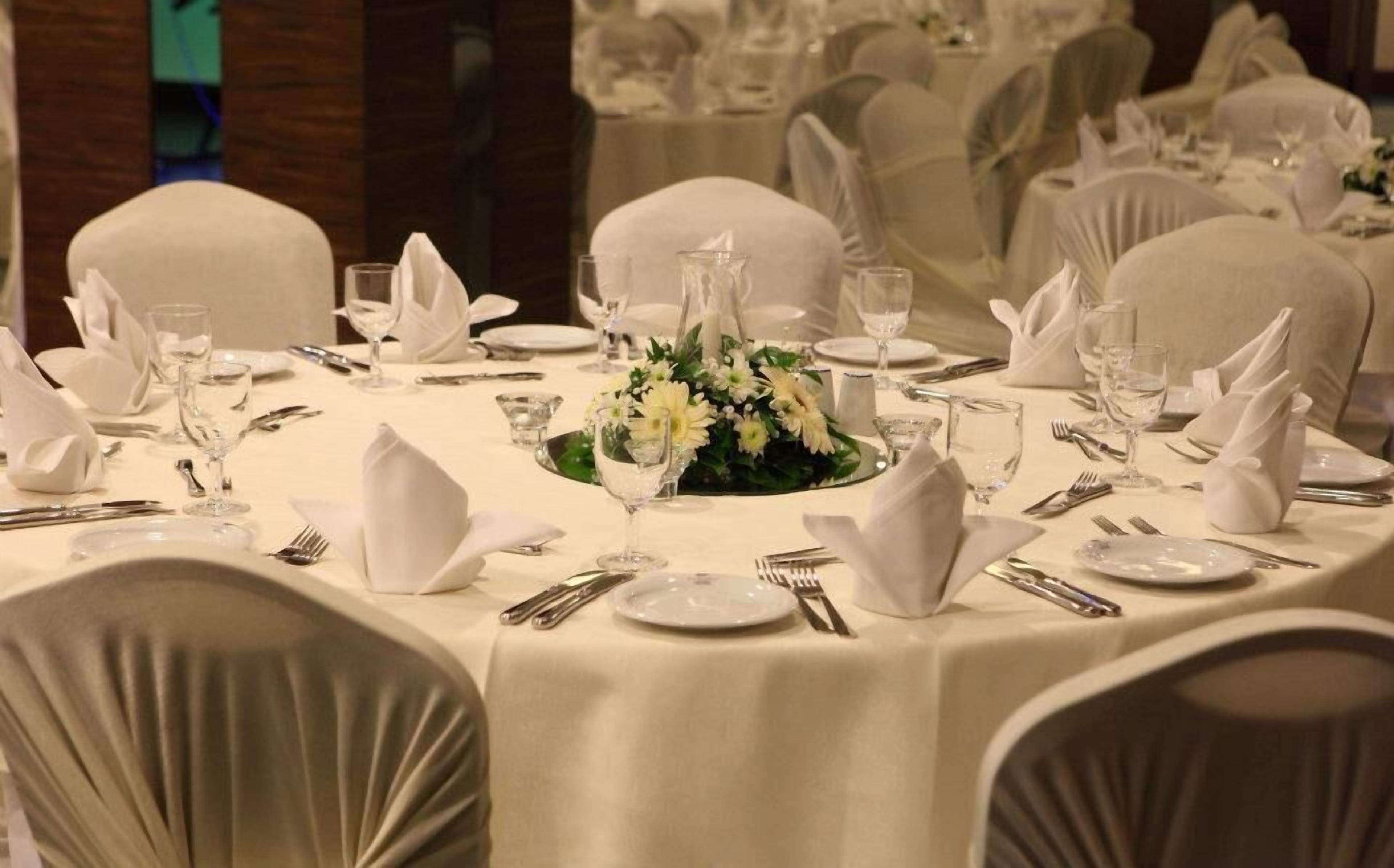 A round dining table set for a formal event, surrounded by chairs with white covers.