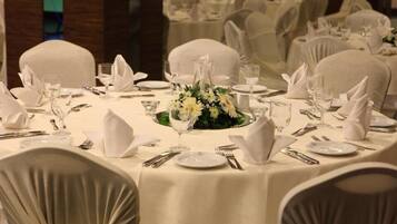 A round dining table set for a formal event, surrounded by chairs with white covers.
