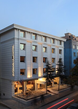 A modern hotel with a light facade, multiple windows, and a visible entrance with outdoor seating. - Eyuboglu Hotel (Ankara)