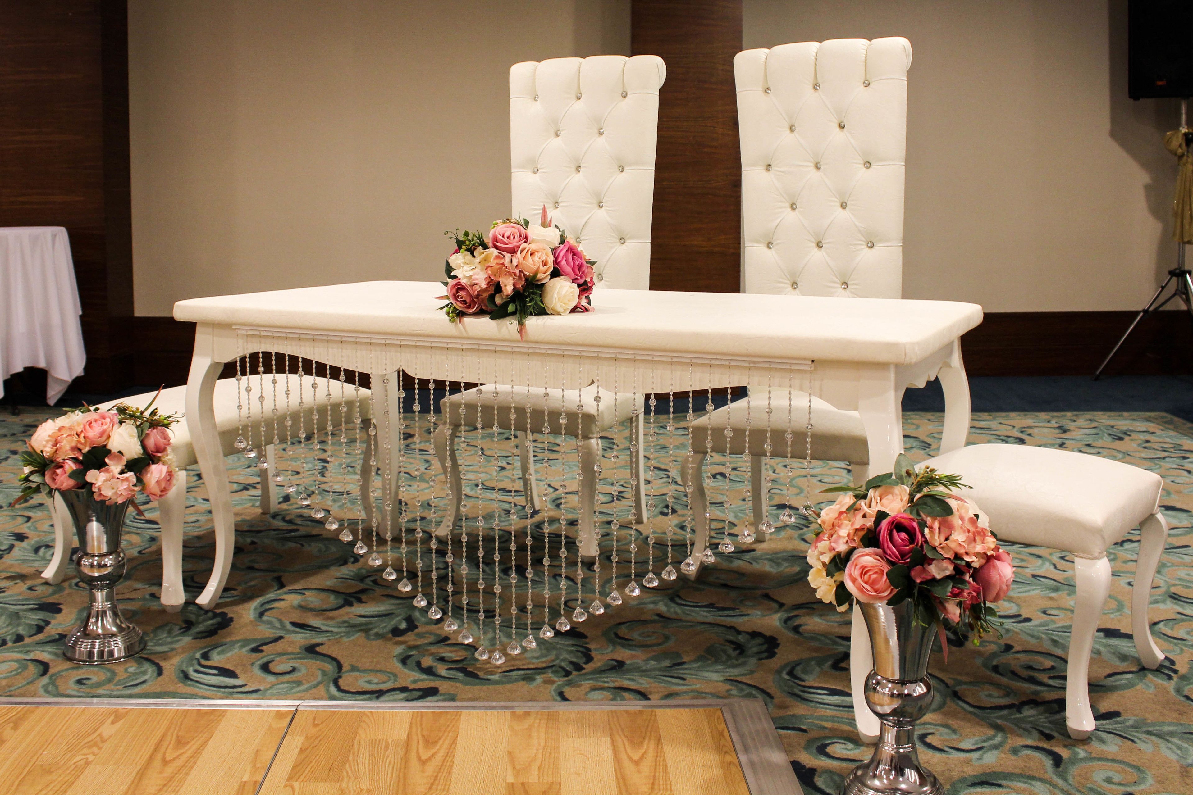 A formal dining table with white upholstered chairs, two vases with flowers, and a decorative hanging centerpiece.