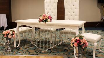 A formal dining table with white upholstered chairs, two vases with flowers, and a decorative hanging centerpiece.