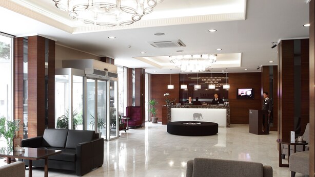Un hall d'hotel modern amb una recepció, zona de seients i grans finestres.