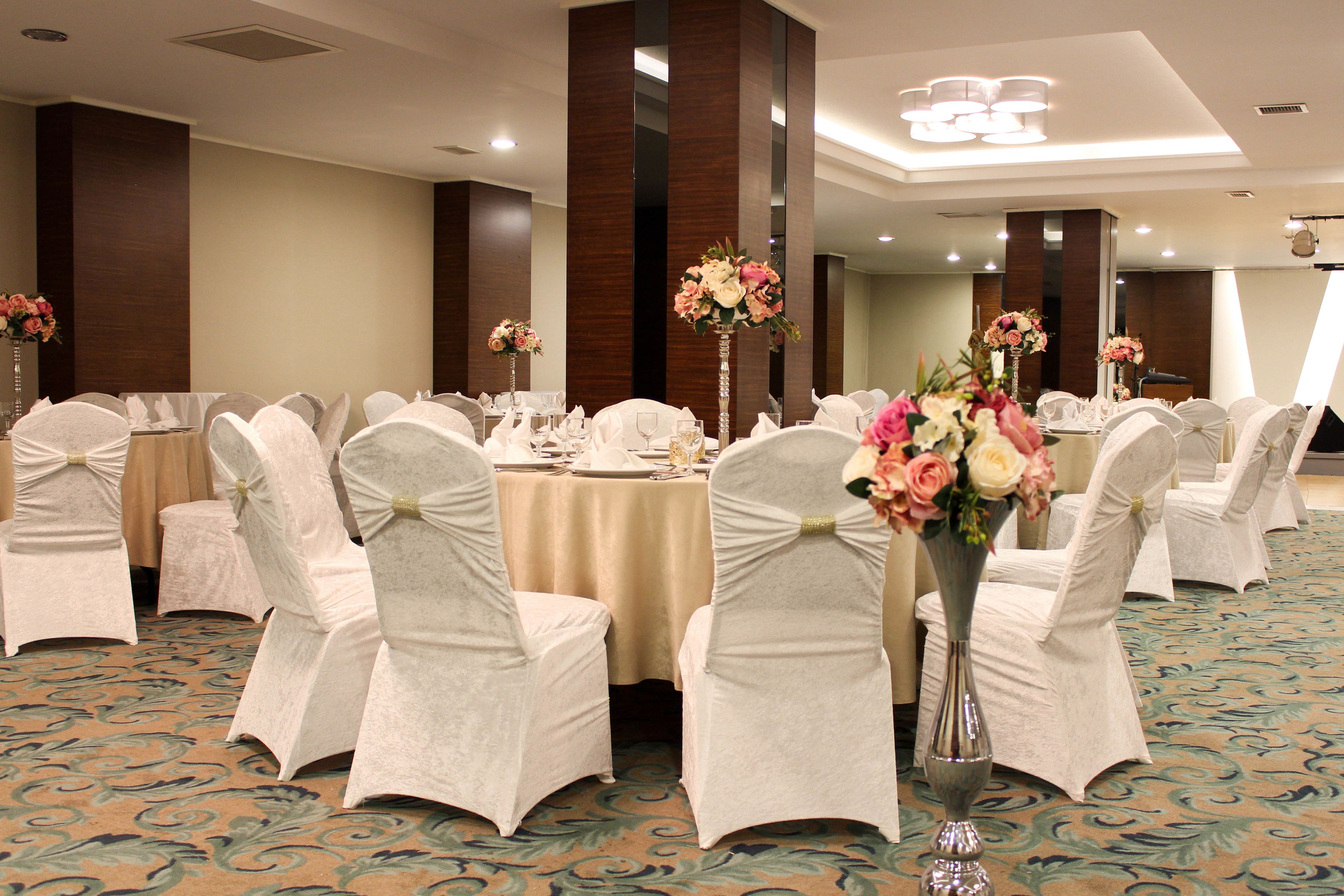 A banquet hall with round tables, white chairs with bows, and floral centerpieces.