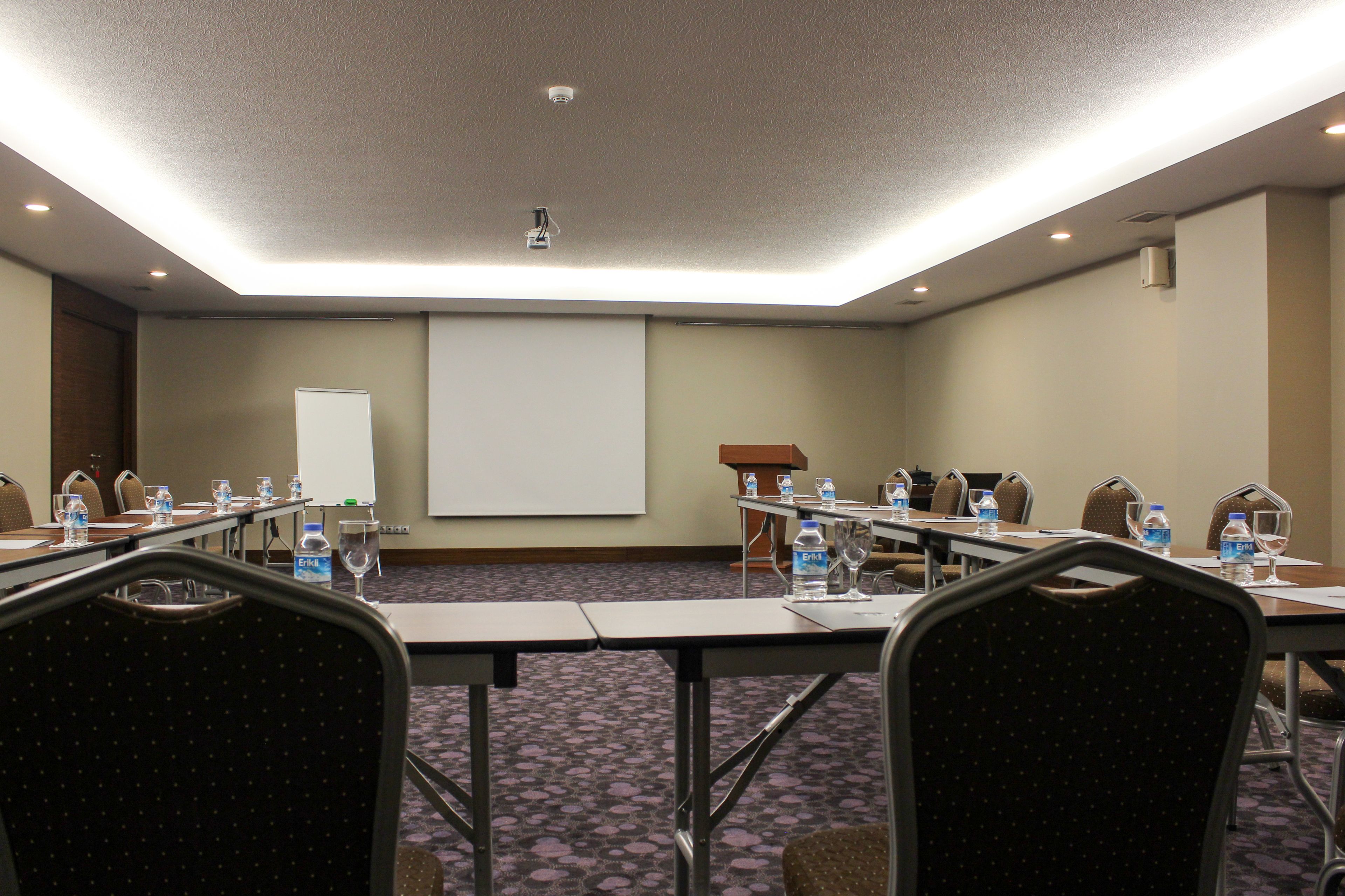 A conference room with a projector screen, tables with water bottles, and chairs.