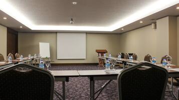 A conference room with a projector screen, tables with water bottles, and chairs.