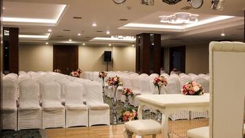 Una sala de banquetes amb files de caires blancs, un escenari amb un orador i centrals florals sobre taules.
