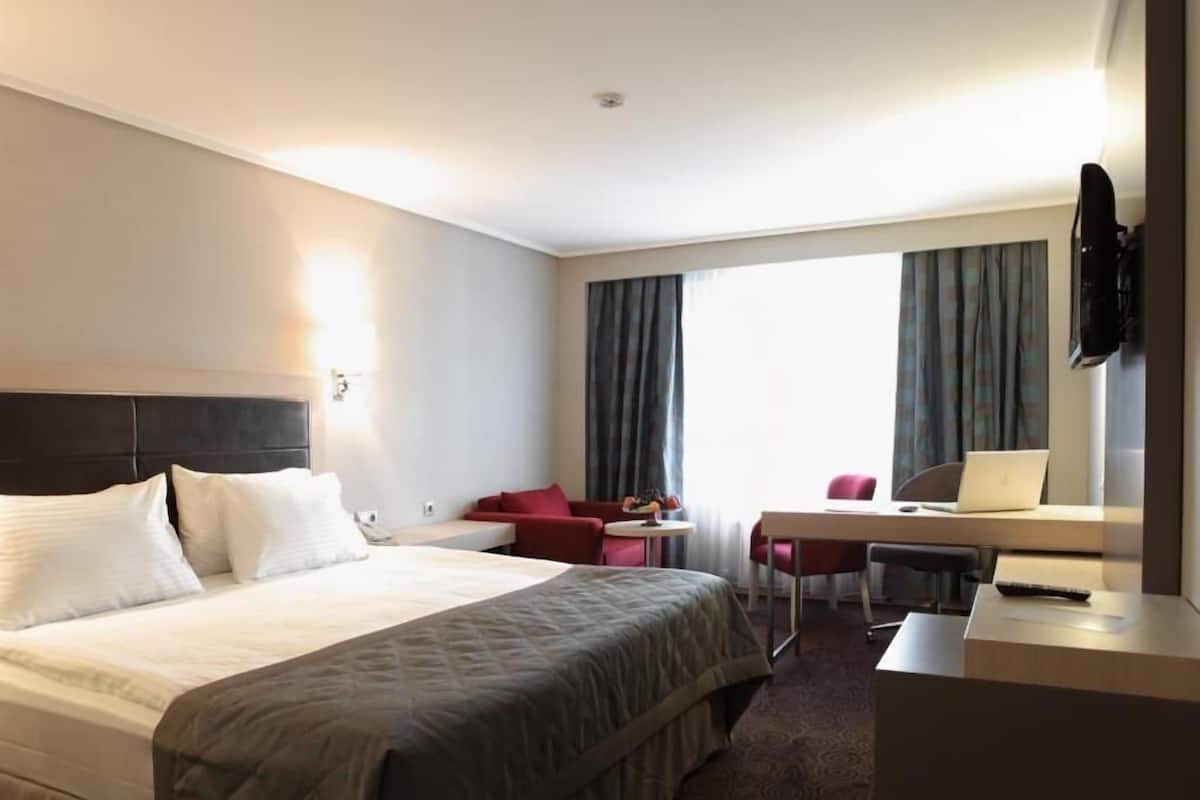 Una habitación de hotel con cama, escritorio con laptop, silla y televisor instalado en la pared.