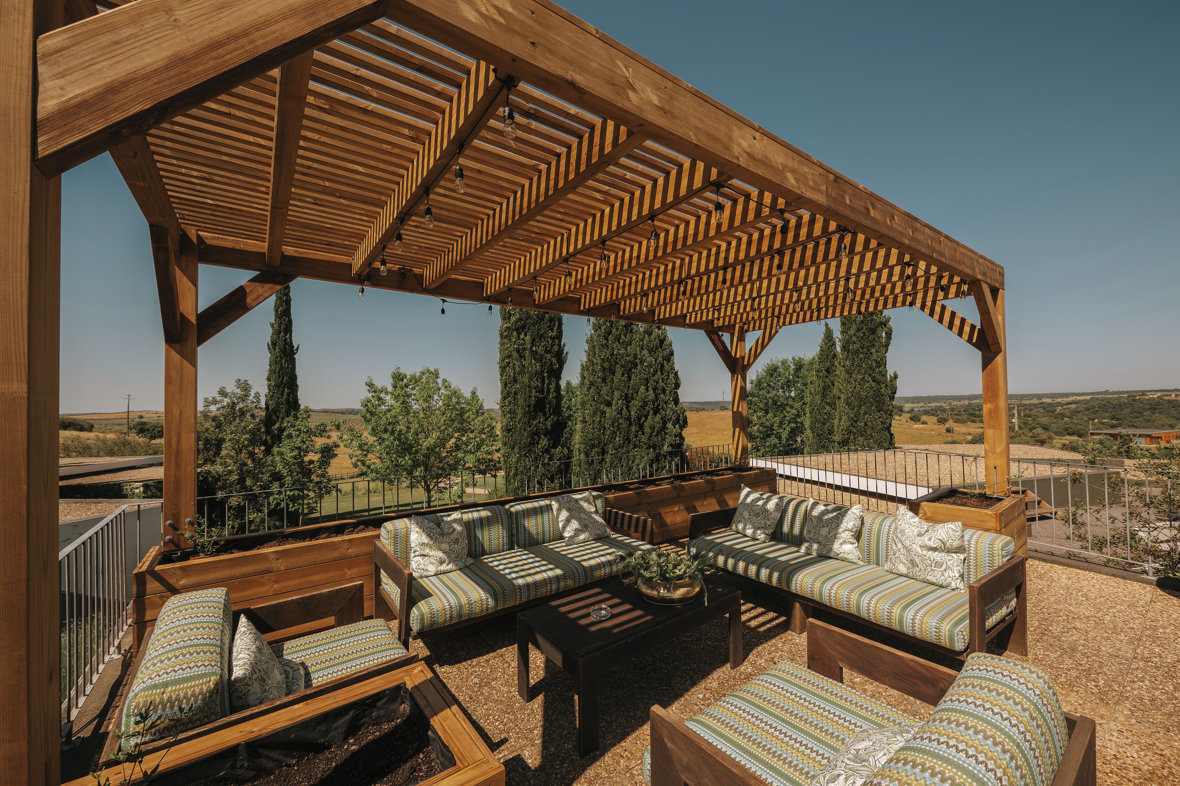 Un espacio de estar al aire libre techado, con mobiliario de madera y vistas al campo.