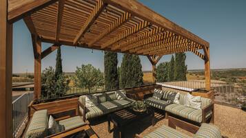 Un espacio de estar al aire libre techado, con mobiliario de madera y vistas al campo.