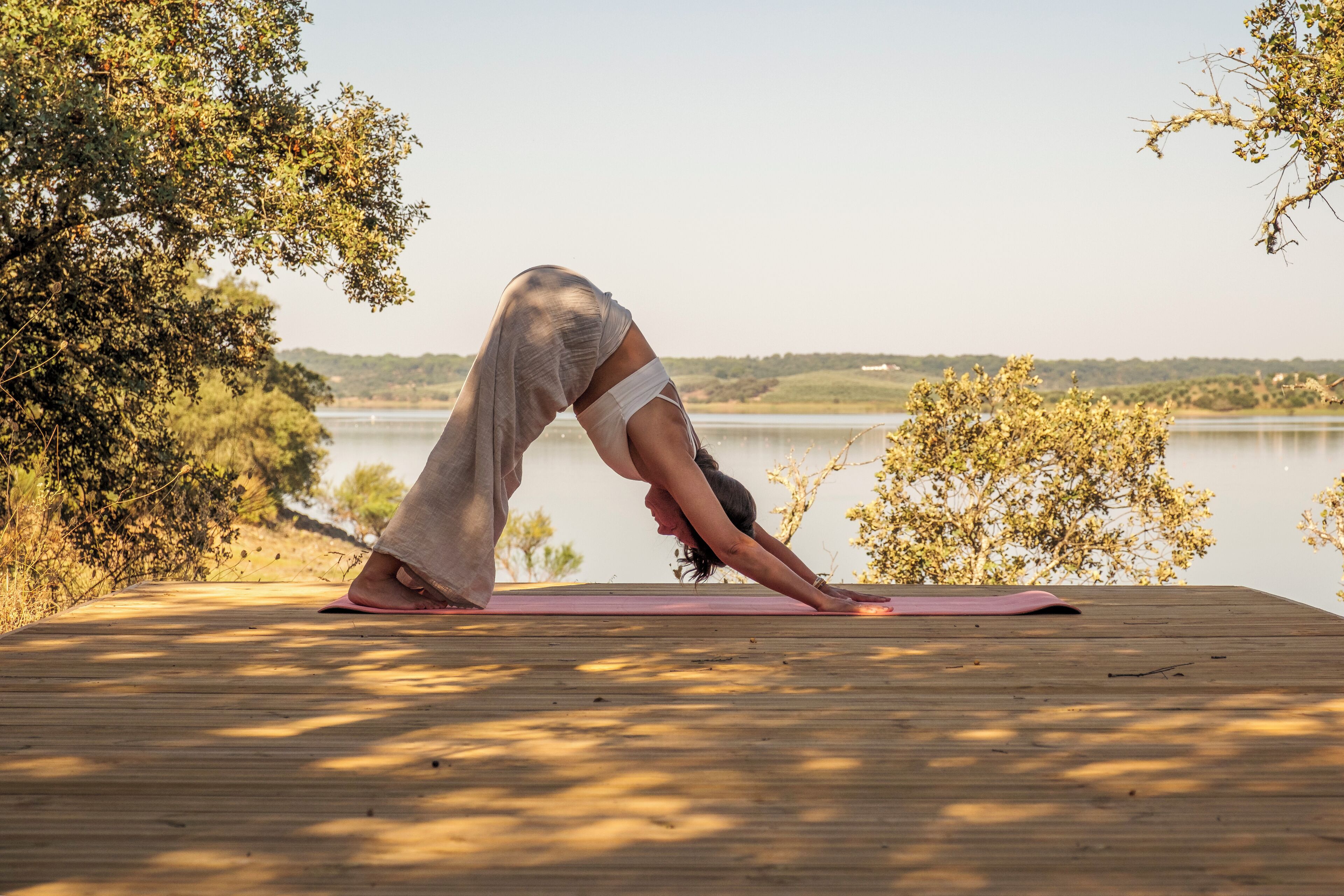 Una persona realiza una postura de yoga sobre una terraza de madera junto a un lago.