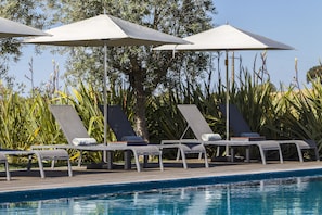 Zona junto a la piscina con sillones de descanso y sombrillas.