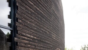Una pareja caminando frente a un edificio moderno con fachada de madera y entrada de vidrio.