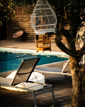 Zona junto a la piscina con sillones de descanso y una jaula colgante.