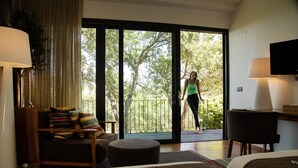 Habitación de hotel con cama, escritorio, silla, sofá y balcón con vista a árboles.