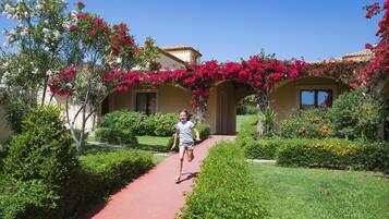A pathway leading to a building with arches covered in pink flowers, surrounded by well-maintained greenery.