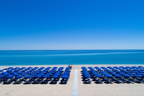 Una playa con hileras de sombrillas y sillas azules, cielo despejado y mar tranquilo.